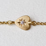 Close-up of the 18k yellow gold bracelet featuring a hand-engraved heart charm with a 2.5mm responsibly sourced diamond set in a star pattern, displayed on a neutral background.