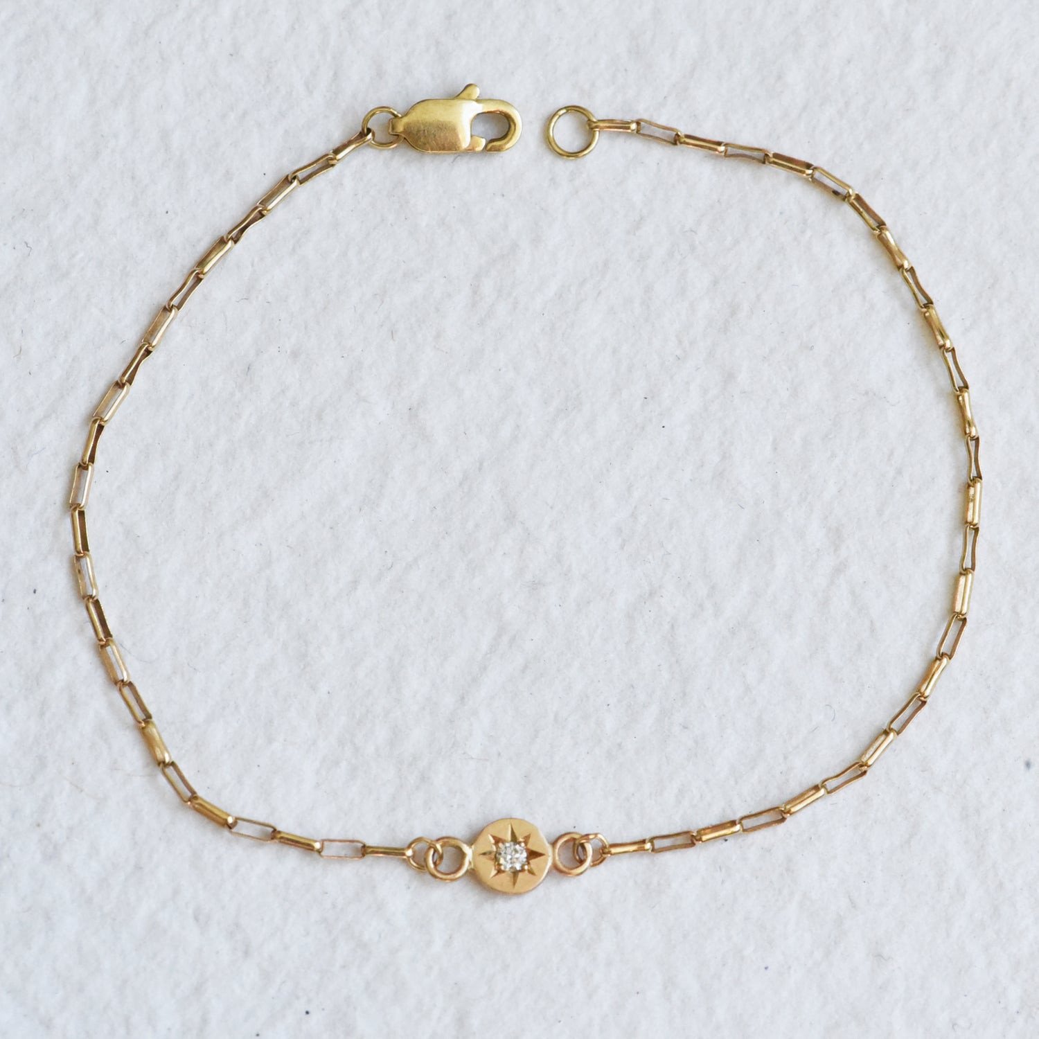Close-up of the solid 14k yellow gold chain bracelet, showcasing hand-engraved details and a diamond set in a classic star setting on a delicate gold chain.
