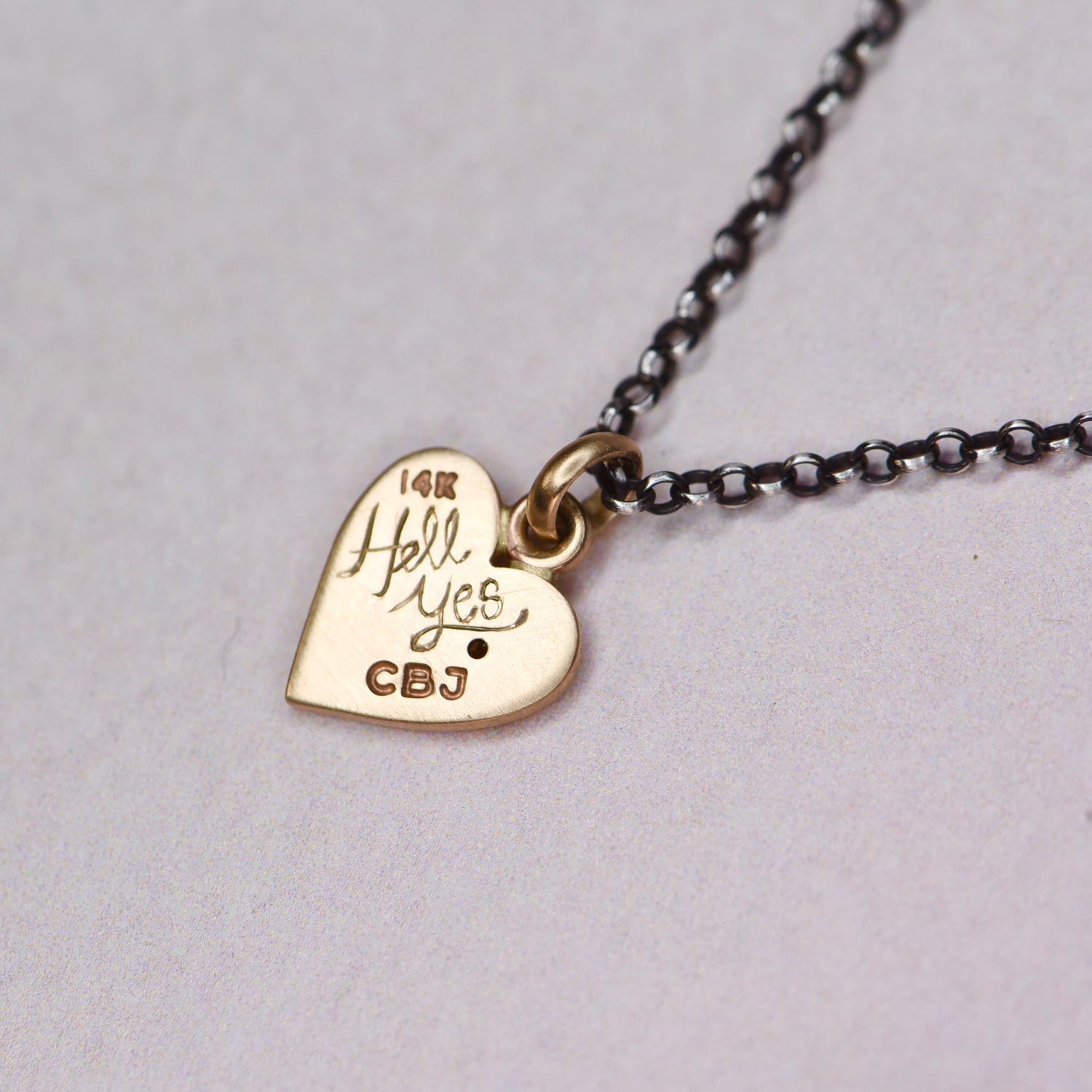 Back view of the 14k gold Misfit Heart pendant hand engraved with “HELL YES,” showing the satin finish and handmade craftsmanship by Corkie Bolton Jewelry.