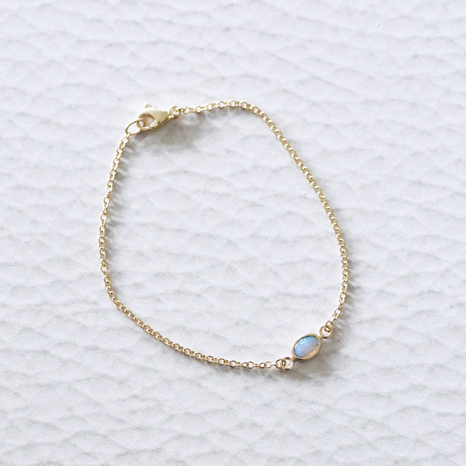 Close-up of the solid 14k yellow gold opal chain bracelet, showcasing a luminous opal set in a delicate gold bezel on a fine gold chain.