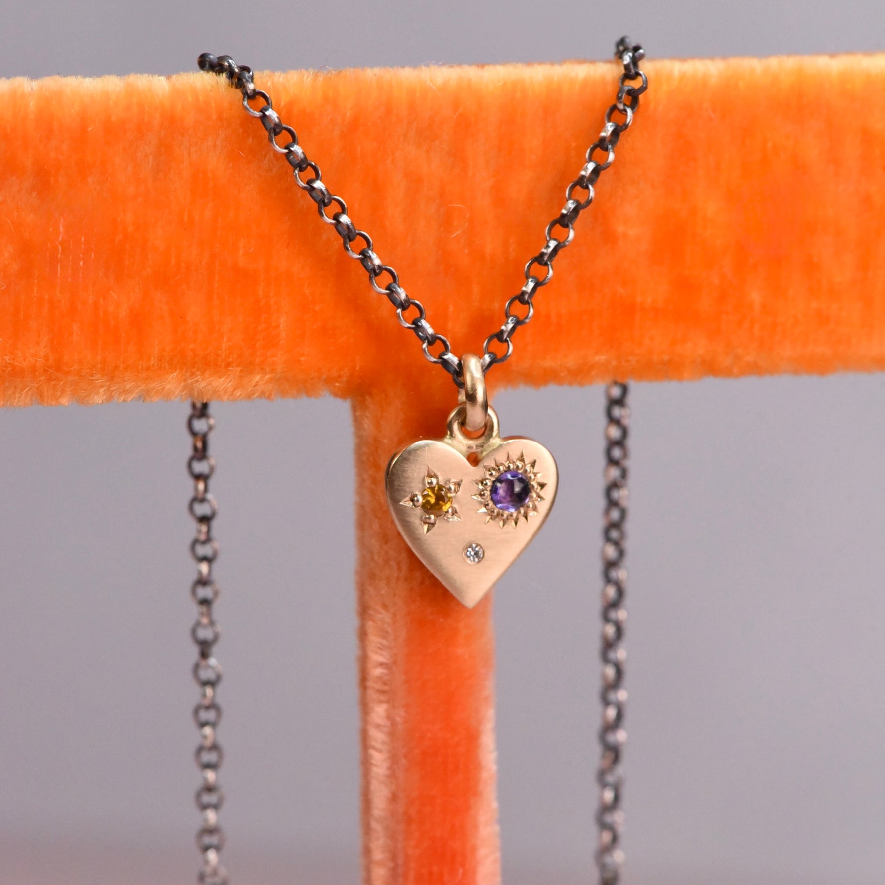 Front view of the handmade 14k yellow gold Misfit Heart necklace featuring a yellow faceted sapphire, a purple cabochon sapphire, and a diamond on an oxidized silver chain by Corkie Bolton Jewelry.