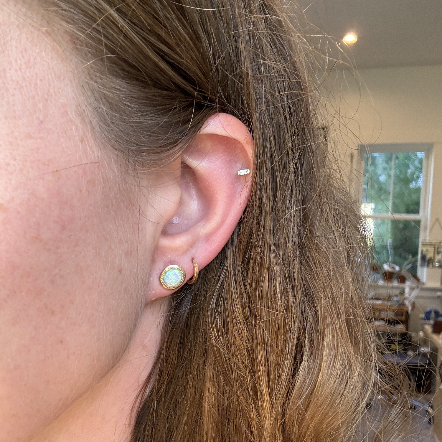 Matte opal gold stud earring styled in a second piercing, paired with other gold jewelry for a chic, layered look.