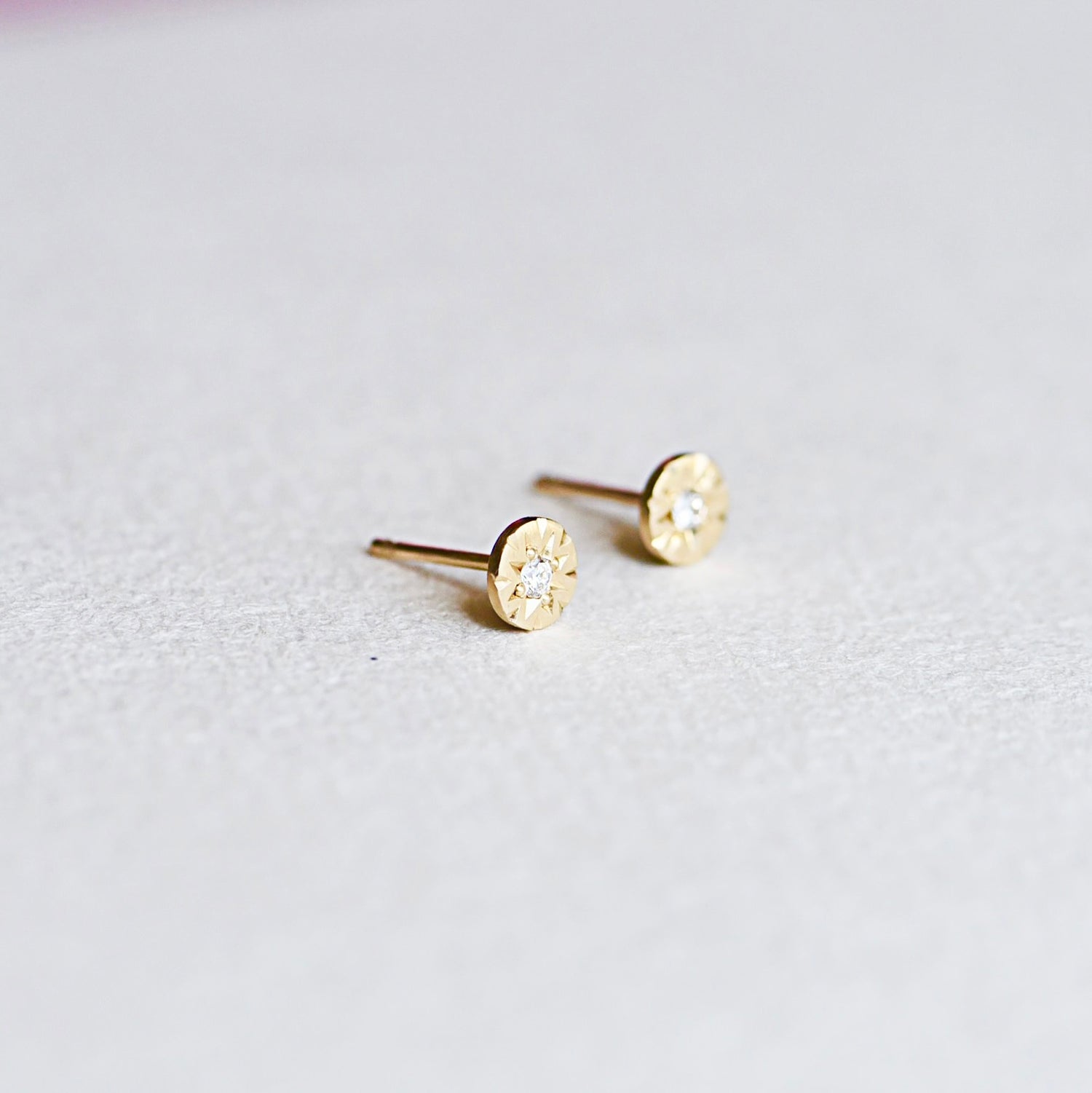 Angled view of 14k gold Funfetti Engraved Diamond studs highlighting engraved cuts and bezel-set diamonds.