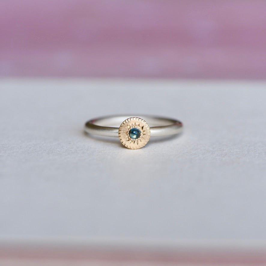 Front view of a handcrafted sterling silver ring with a 14k yellow gold bezel-set blue sapphire and hand-engraved starburst details by Corkie Bolton Jewelry.