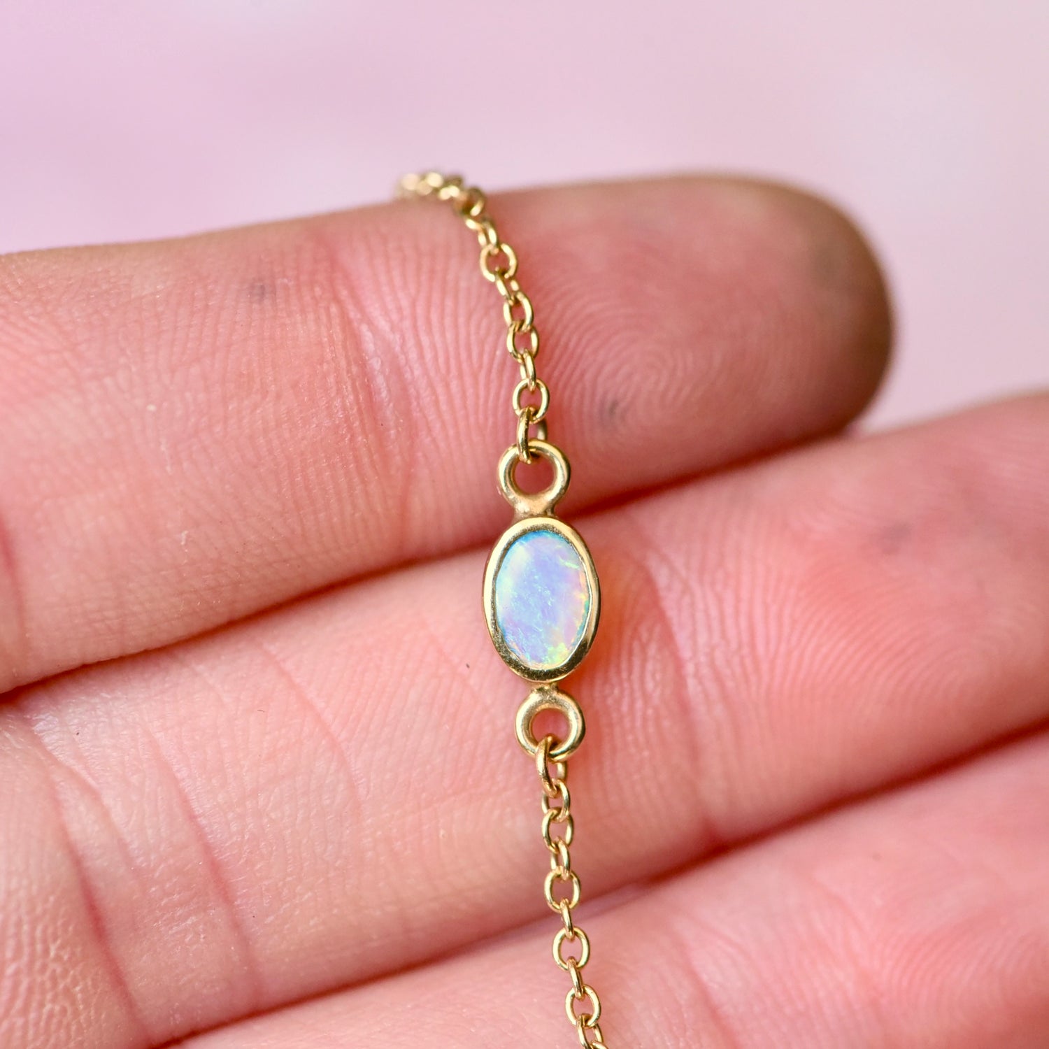 Close-up of oval opal gemstone set in solid 14k gold cable chain bracelet.