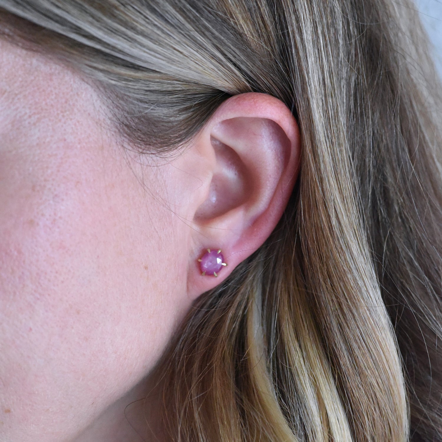 (Lifestyle shot): Fierce Pink Sapphire Studs in 18k Gold worn on ear, adding a pop of vibrant pink to a minimalist look.