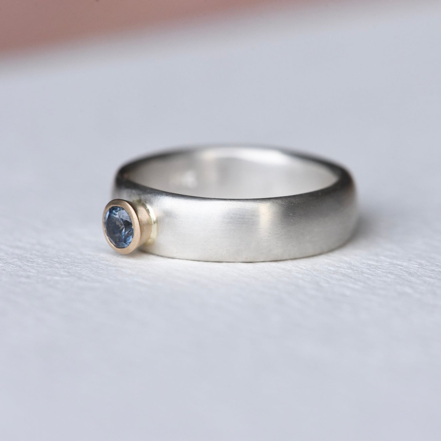 Side profile of Montana sapphire ring with 14k gold bezel and satin-finished sterling silver band, showcasing artisan craftsmanship.