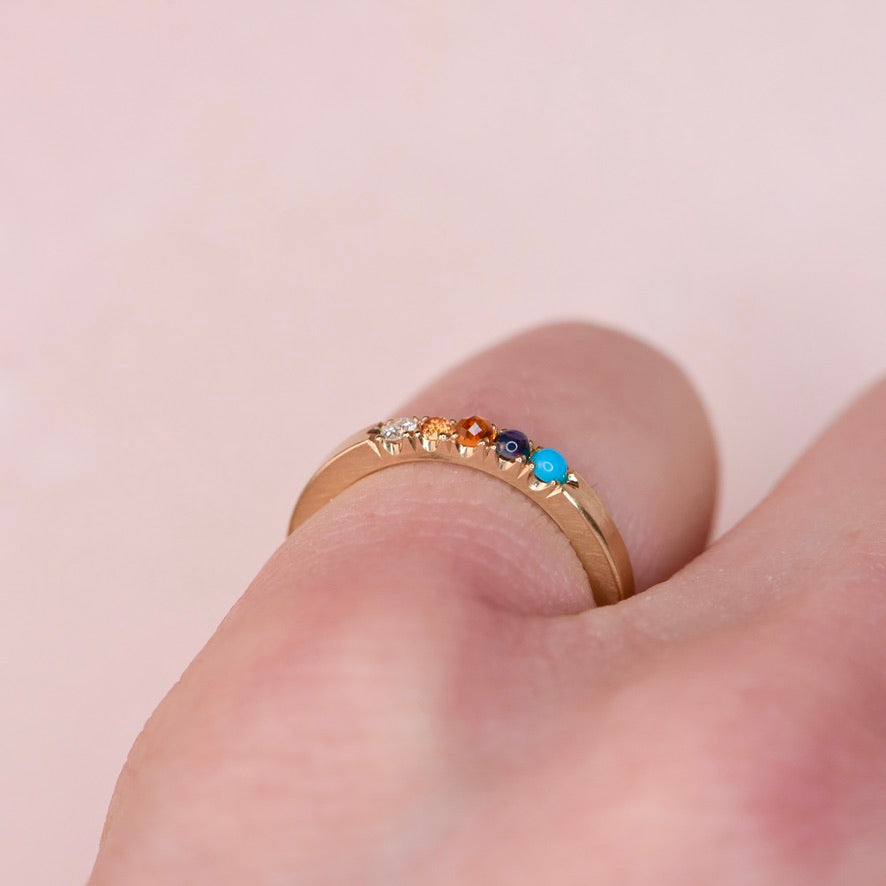 Side view of 10k yellow gold five stone castle set ring with turquoise sapphire and diamond worn on finger