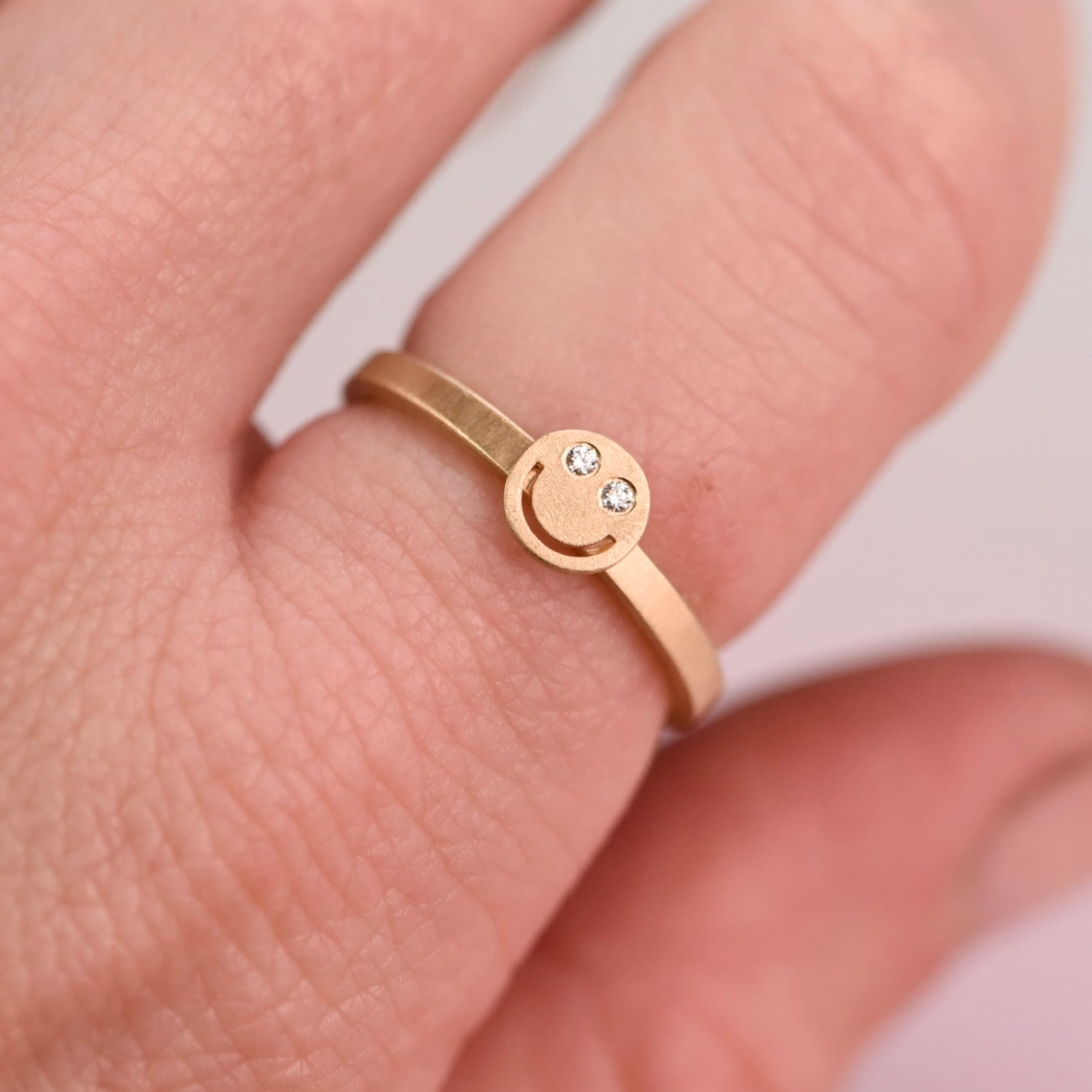 Artisan jeweler’s 10 K yellow gold ring size 7 featuring a smiley face design with responsibly sourced diamonds. Modeled on a hand.