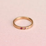 Top view of a 14k yellow gold ring featuring two pink sapphires and a misfit diamond in hand-engraved star settings, designed by Corkie Bolton Jewelry.