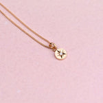 Flatlay of a 14k gold necklace featuring a hand-engraved star-set diamond charm on a curb chain against a soft pink background