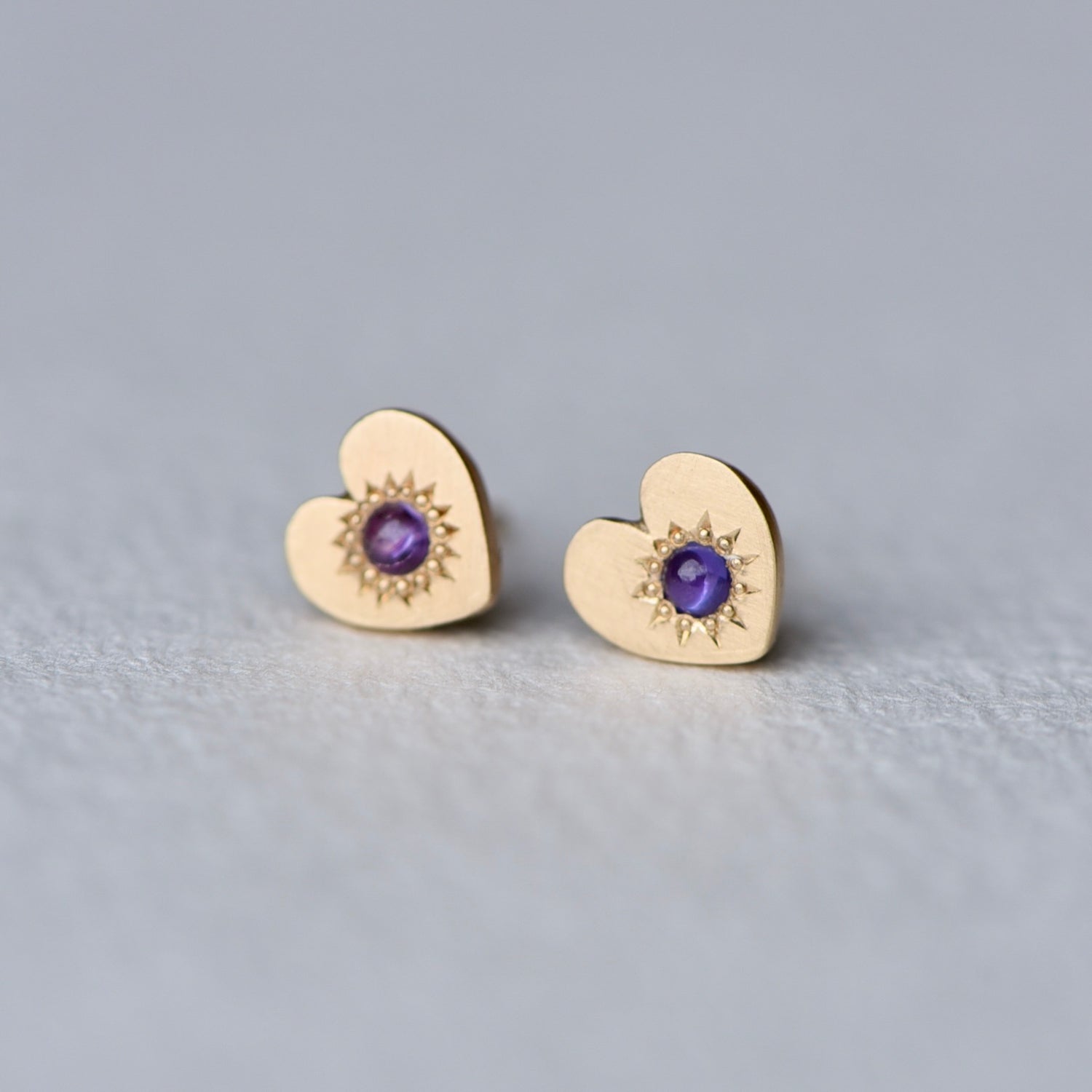 Heart-shaped gold earrings with purple gemstones on a light gray background