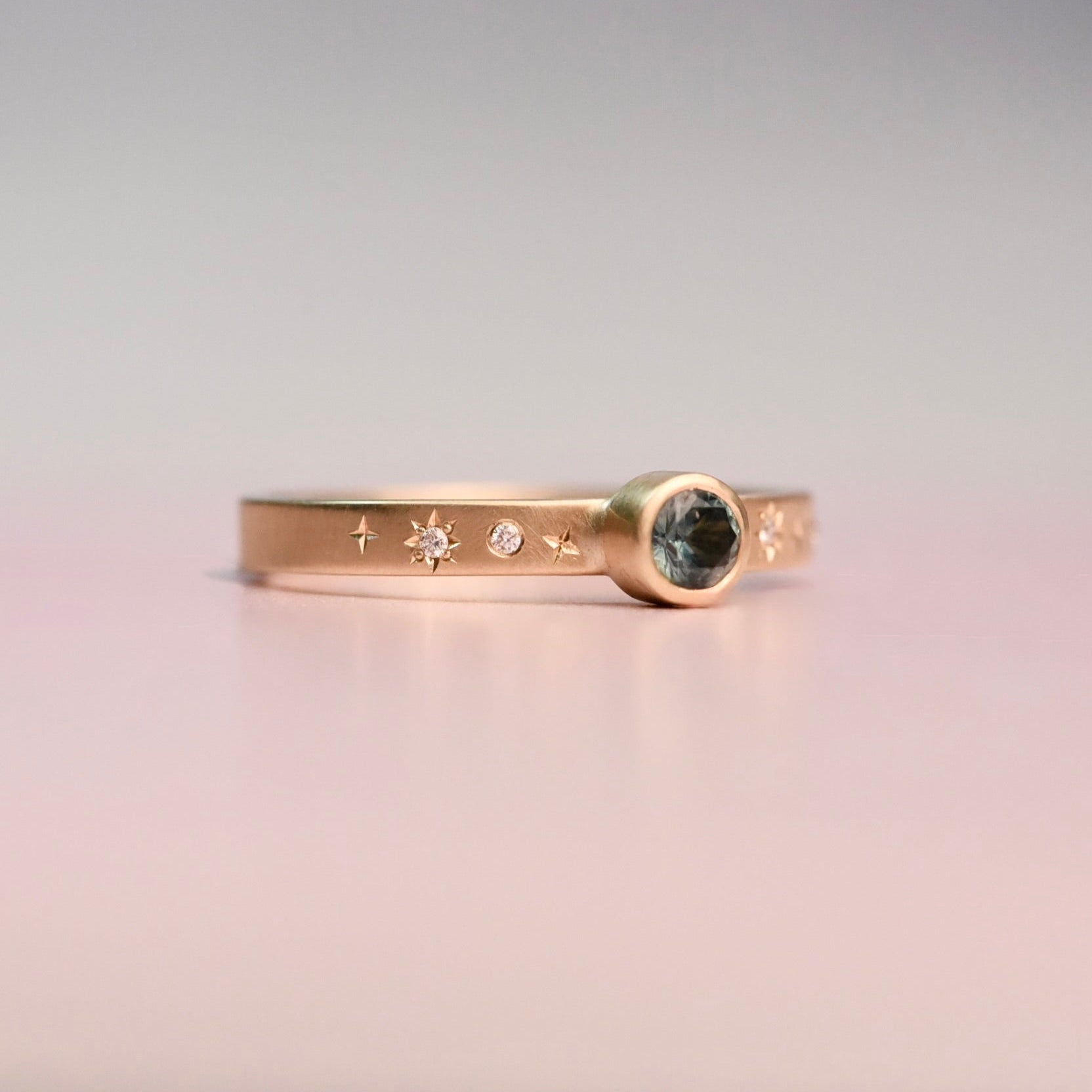 Gold ring with gemstone and star designs on a gradient background