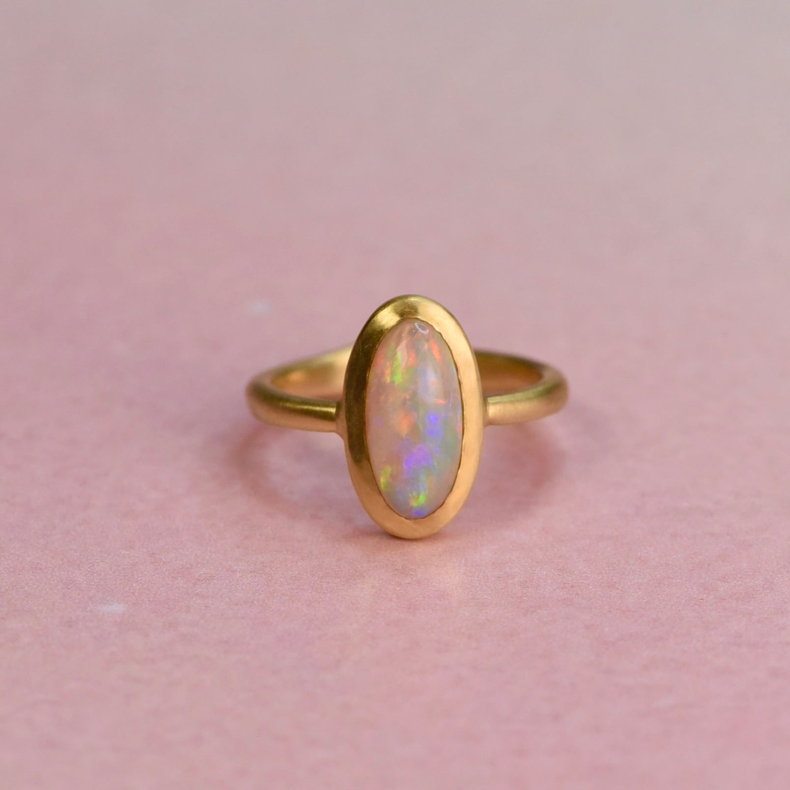Gold ring with an opal stone on a pink background