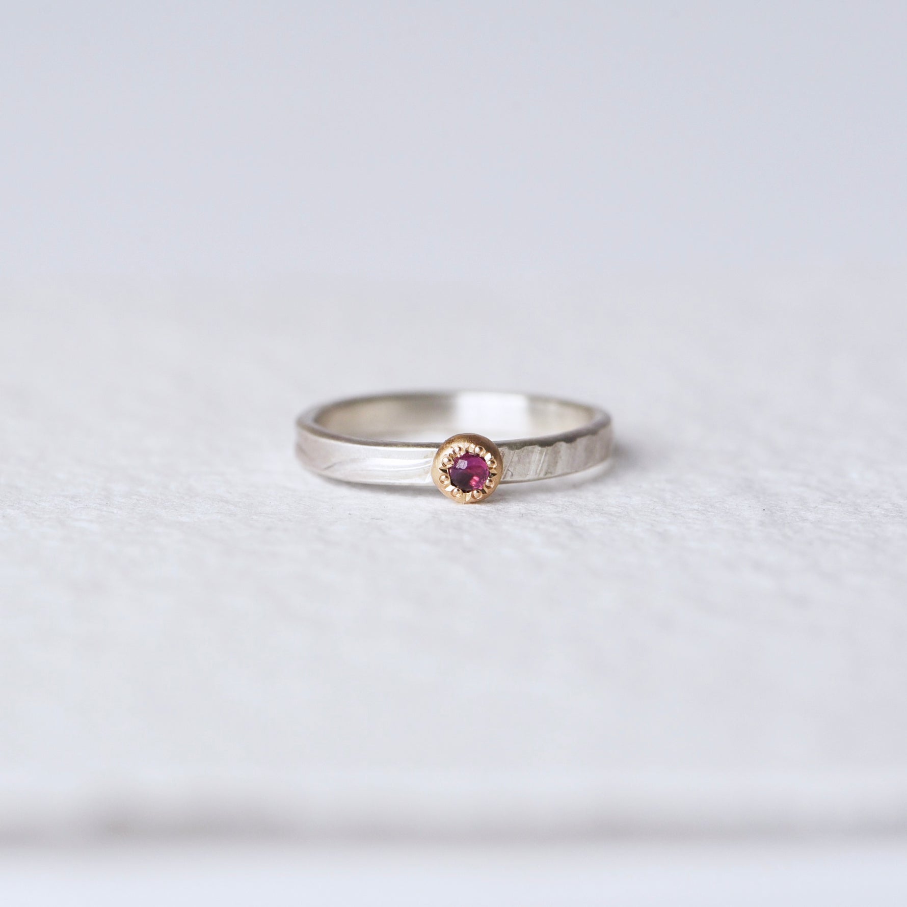 Front view of pink sapphire ring: A front-facing image showcasing a pink "berry" sapphire cabochon set in a 14k yellow gold engraved bezel, mounted on a satin-finished sterling silver band with an abstract floral texture.