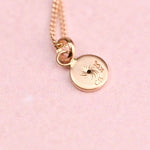 Gold necklace with a round pendant on a pink background