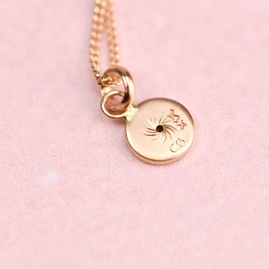 Gold necklace with a round pendant on a pink background