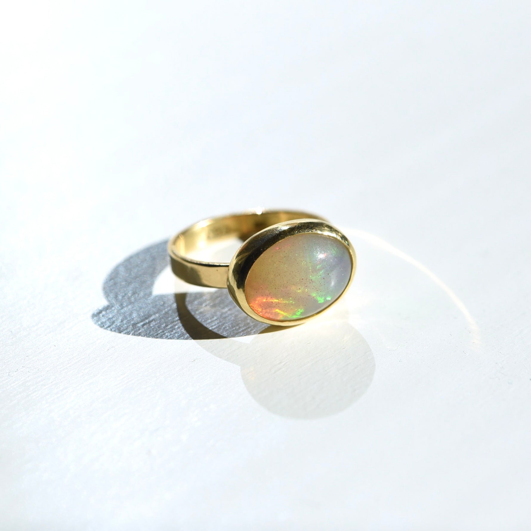 18k and 22k Gold Opal Ring on a white background, featuring a vibrant opal with flashes of blue and green, set in a rich yellow gold bezel.