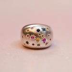 Silver ring with multicolored gemstones on a light pink background