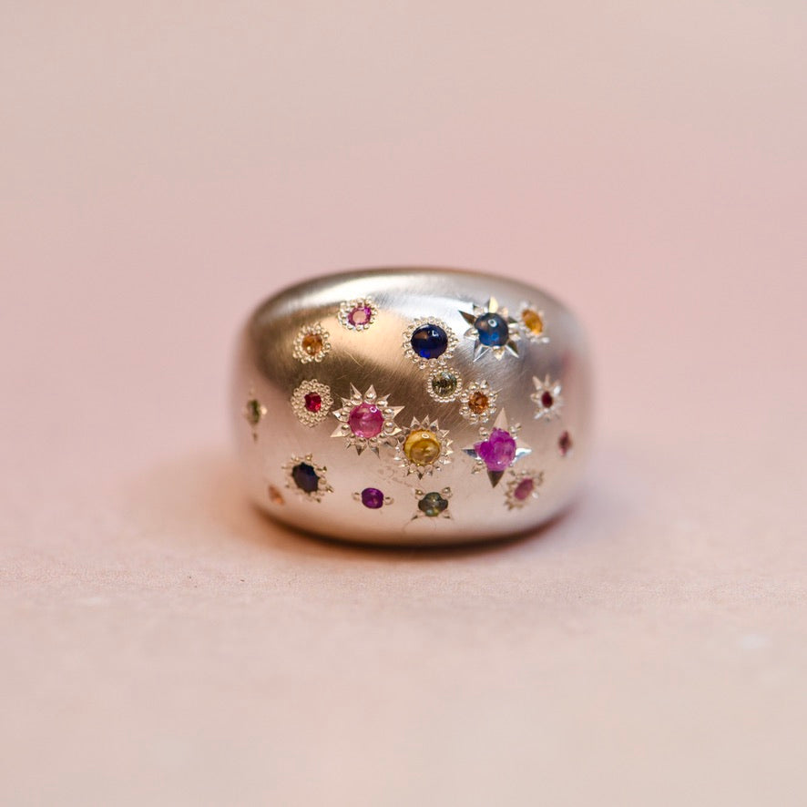 Silver ring with multicolored gemstones on a light pink background