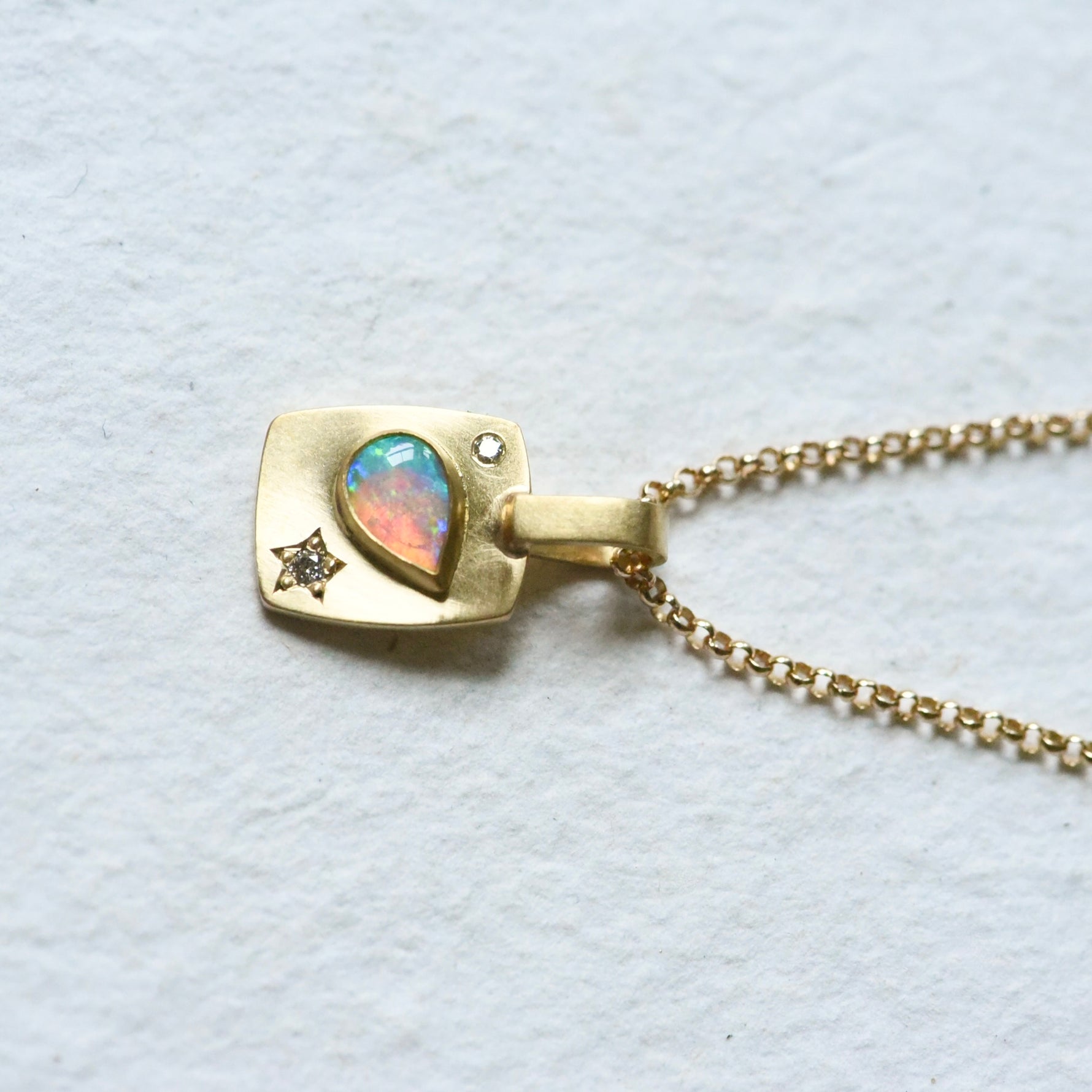 On a chain,  !8k yellow gold rectangular charm with a pear shaped Coober Pedy Australian Opal and diamonds. Hand engraved.