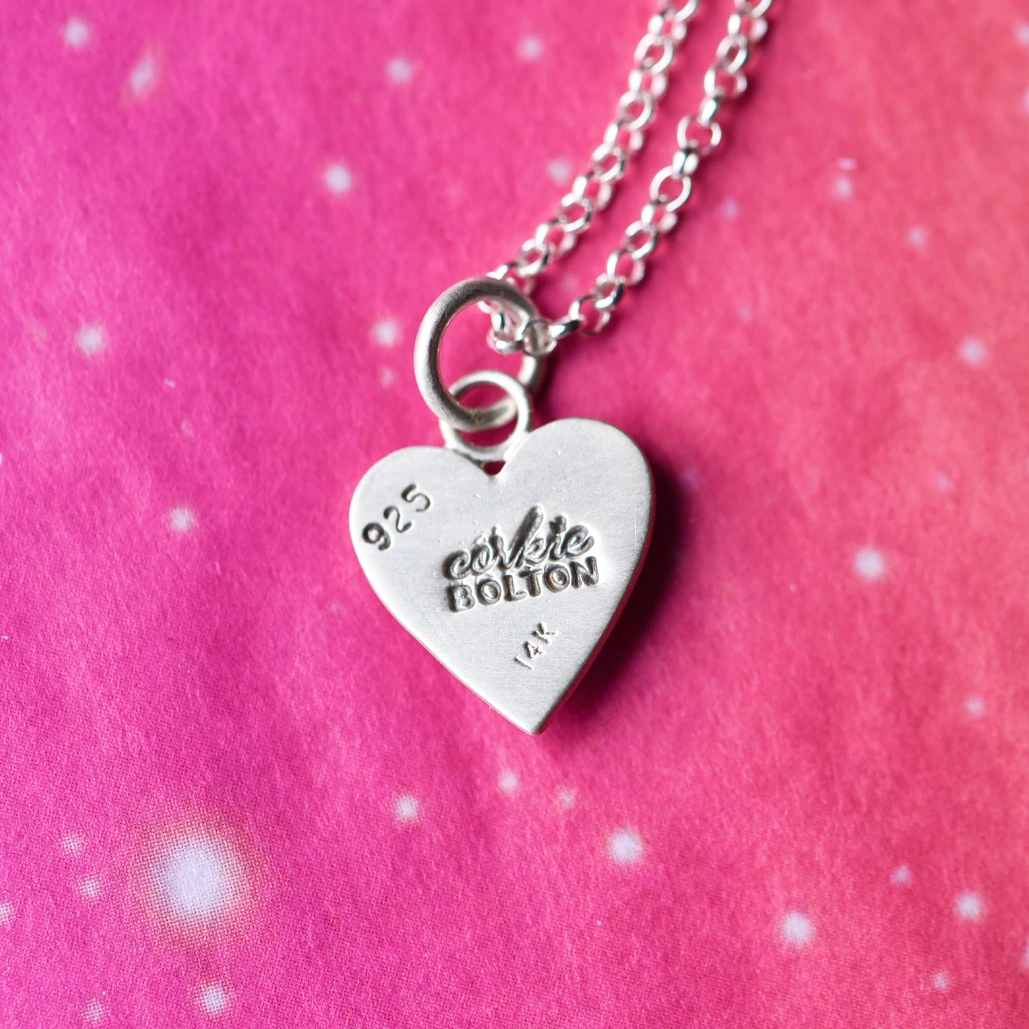 Back view of the silver heart charm with visible matte finish and hand-stamped 14k + CB maker’s mark.