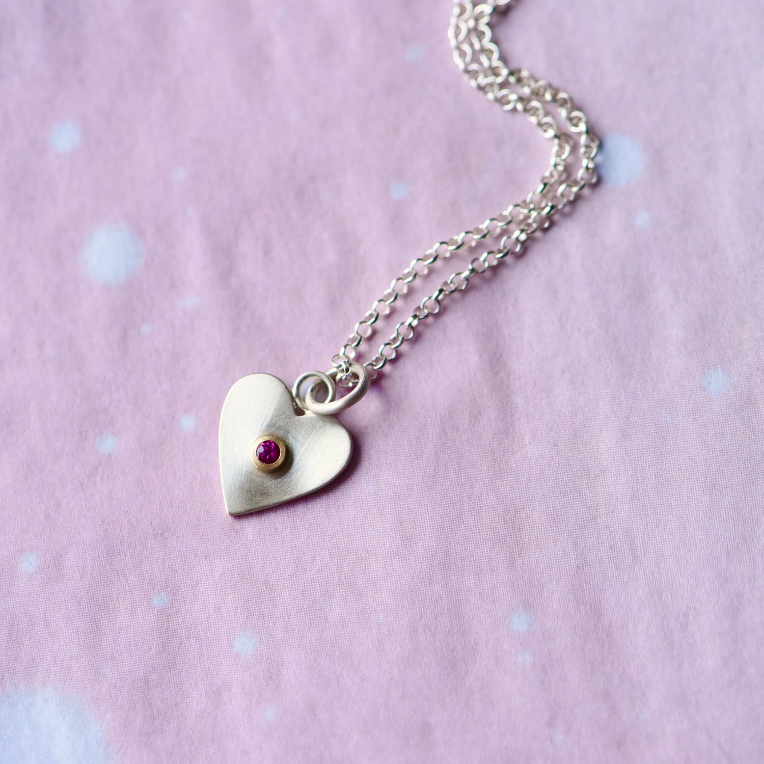 Sterling silver heart necklace with a hot pink sapphire set in a 14k gold bezel on a white background.