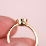 Close-up of a teal diamond in a hand engraved star setting on the side of a thick 14k yellow gold bezel