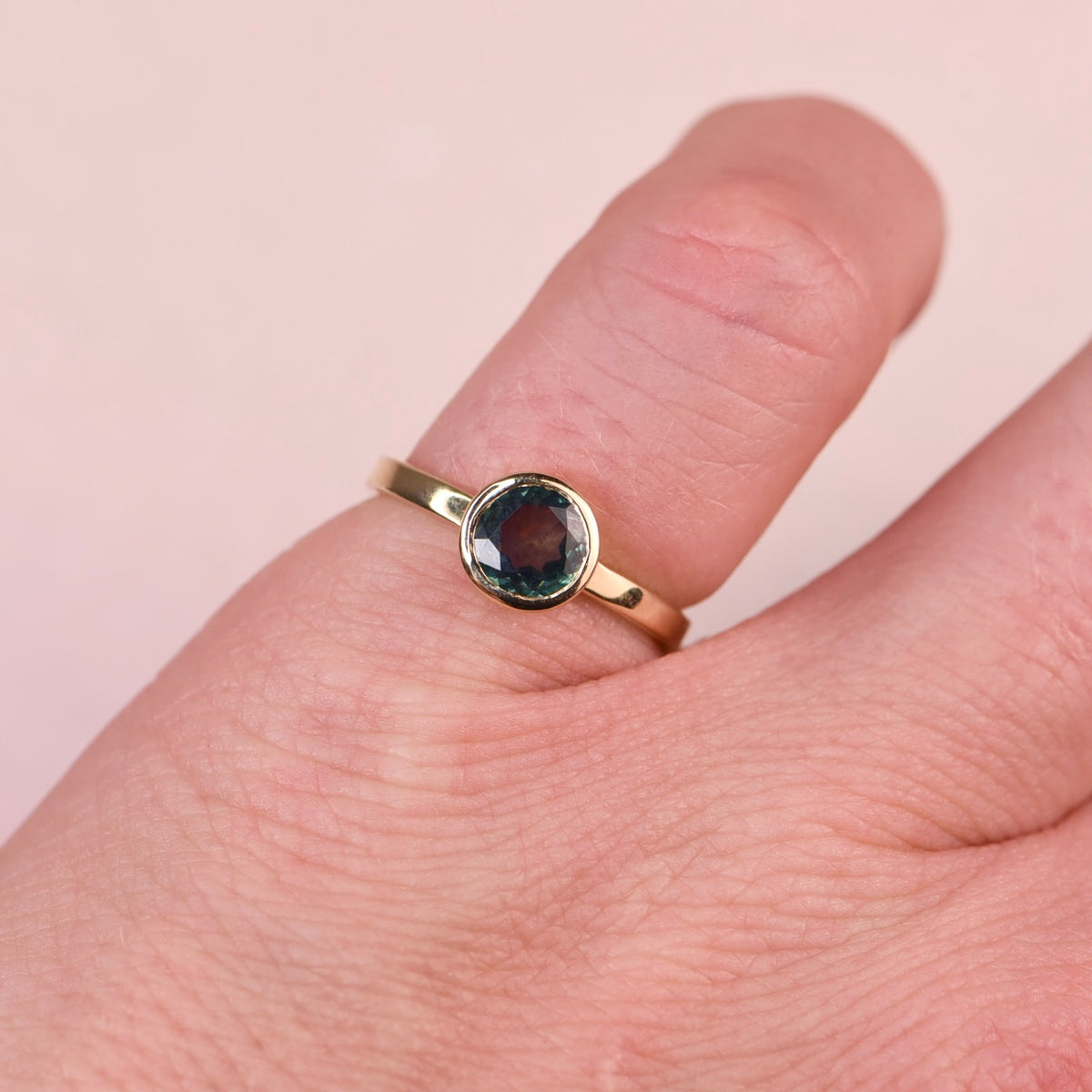 Teal sapphire gold ring in a 14k yellow gold bezel worn on a finger