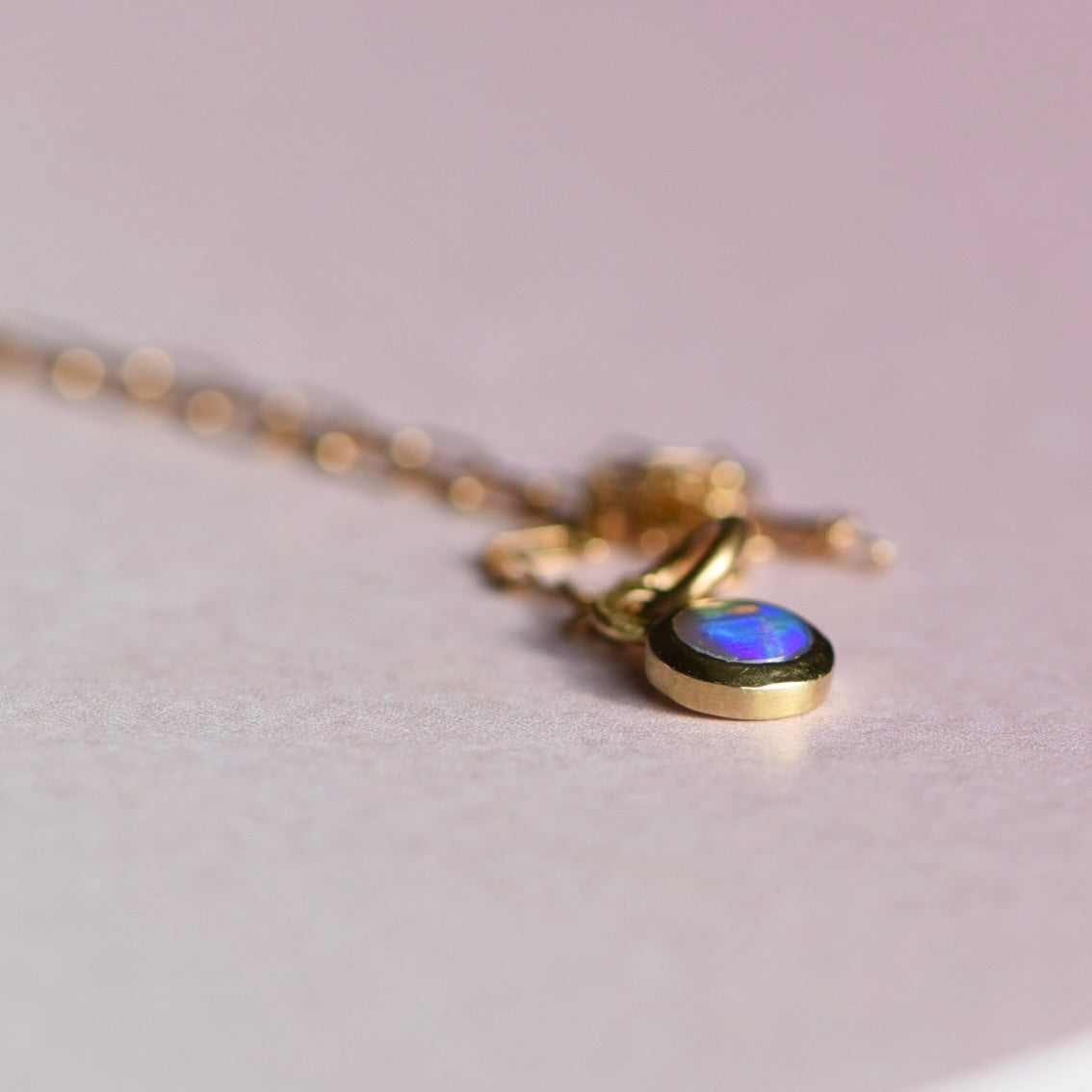 Gold necklace with an opal pendant on a light gray background