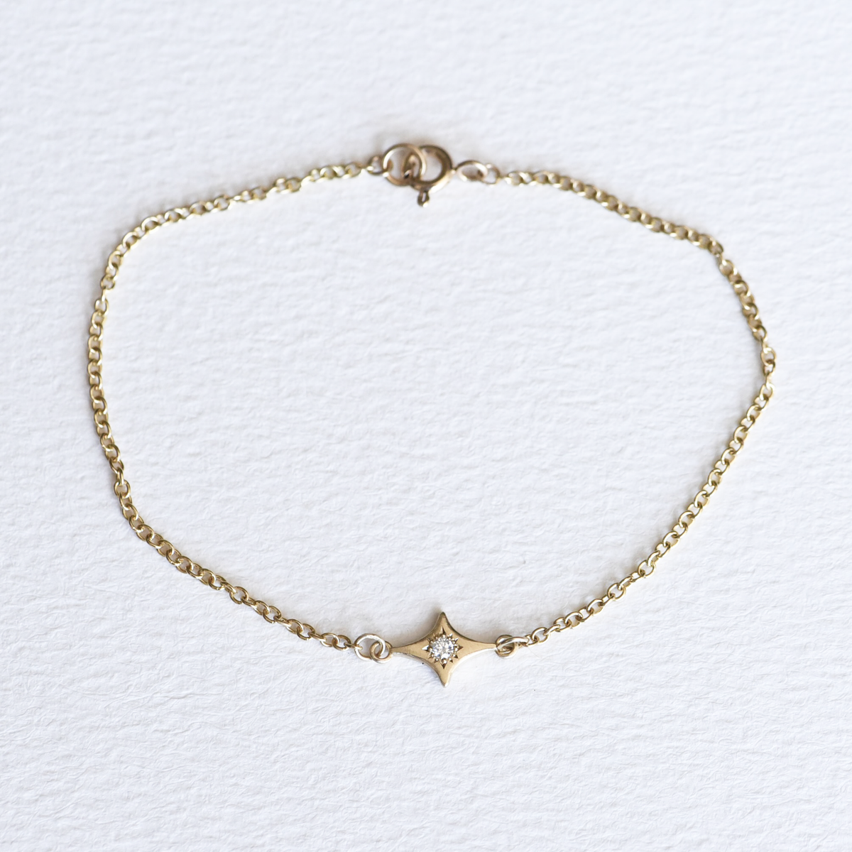 A 14k yellow gold cable chain bracelet with a sparkle charm and diamond engraving, displayed against a white background.
