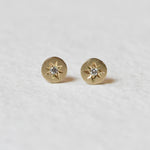 Close-up of Celestial Diamond Studs on a White Background – A pair of small, delicate diamond studs set in gold with a starburst design. Each stud features a sparkling round diamond in the center, surrounded by fine, textured details that give a celestial look.