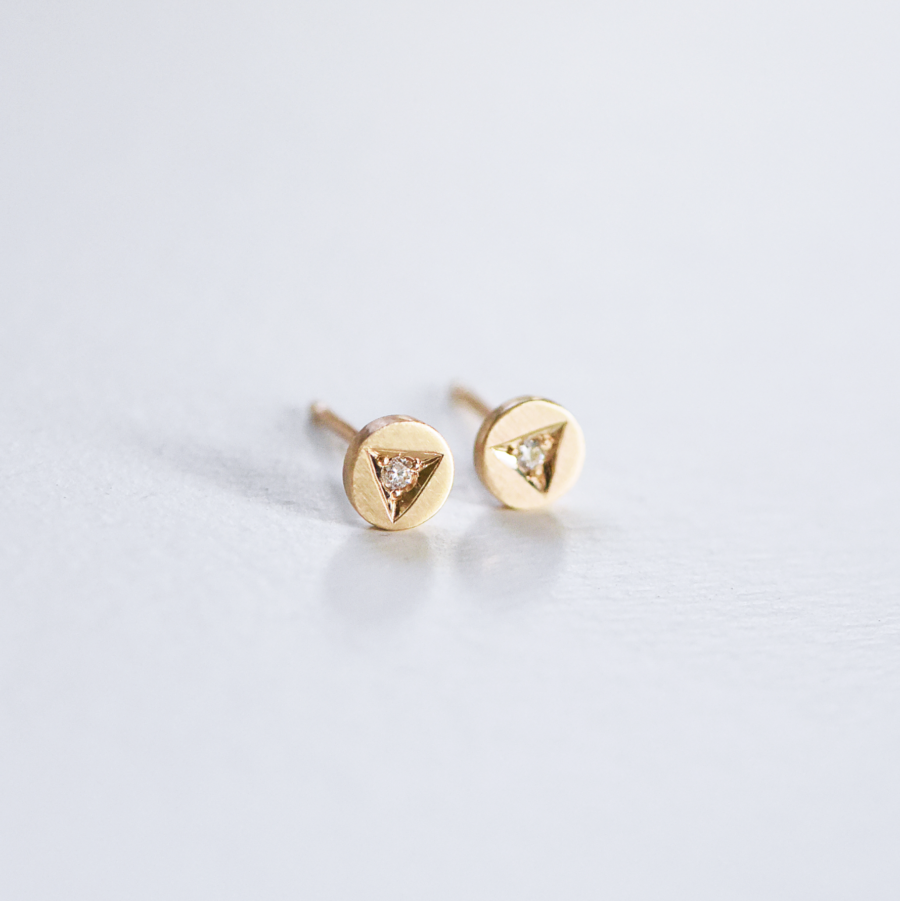 Handcrafted 14k gold diamond stud earrings by Corkie Bolton Jewelry featuring unique triangle engravings. These artisan-made earrings highlight delicate, hand-engraved details with a sparkling diamond centerpiece in each stud, blending minimalism with fine craftsmanship for a timeless design.