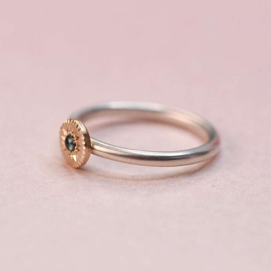 other side view of a sterling silver ring with a 14k gold engraved disc and blue sapphire center stone, photographed on a soft pink surface.