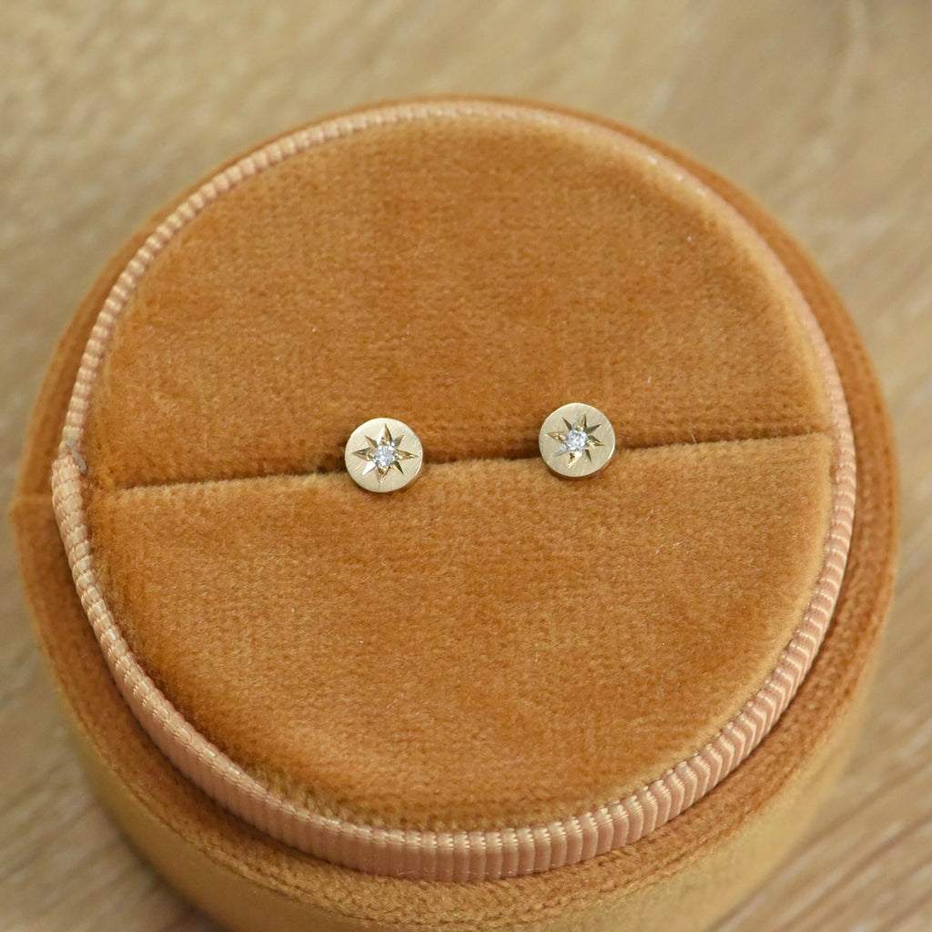 Celestial Diamond Studs Displayed on a Jewelry Stand – Two diamond-studded earrings with a gold starburst design, neatly displayed on a beige jewelry stand. The elegant, minimalist design of the earrings is highlighted.