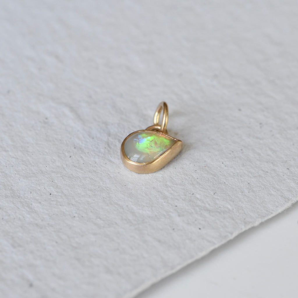 A teardrop flashy opal set in 14k gold as a charm, created by Corkie Bolton Jewelry.