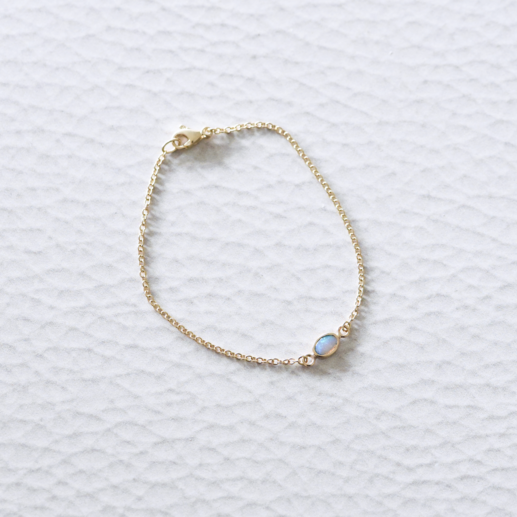 Close-up of the solid 14k yellow gold opal chain bracelet, showcasing a luminous opal set in a delicate gold bezel on a fine gold chain.