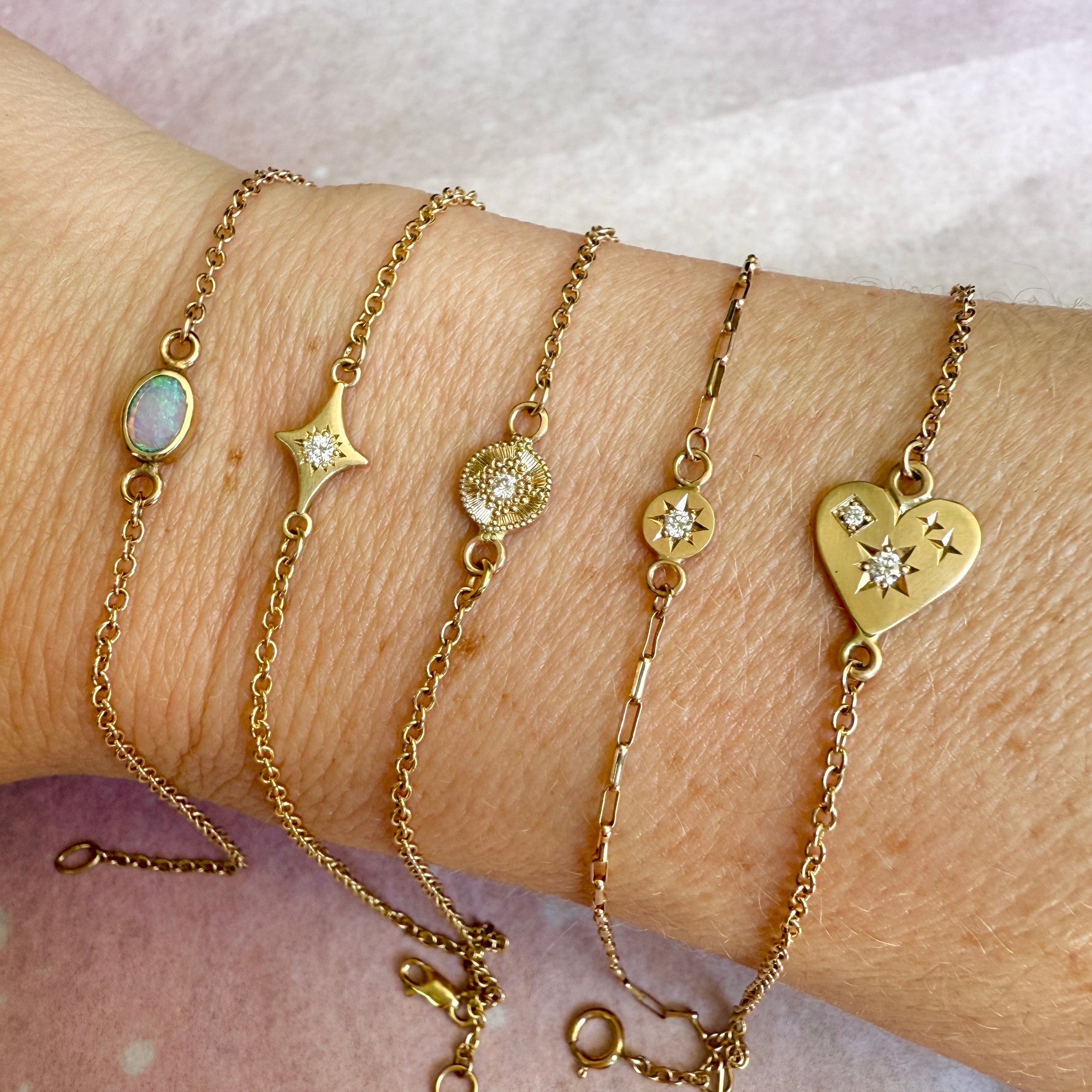 Gold bracelets with various charms on a wrist against a white background