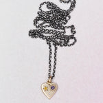 Full view of the handmade HELL YES Misfit Heart Necklace by Corkie Bolton Jewelry, featuring a 14k yellow gold heart pendant with yellow and purple sapphires and a diamond on an oxidized sterling silver rolo chain.