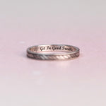Silver ring with engraved text on a light pink background