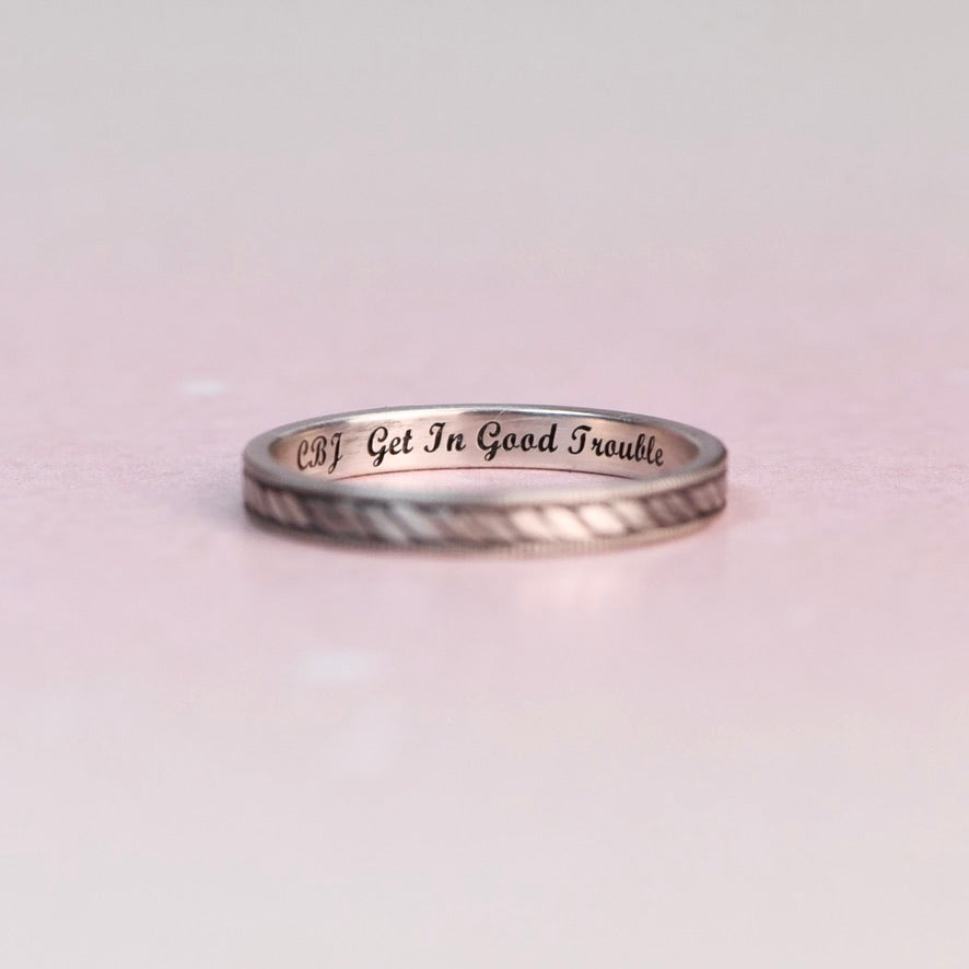 Silver ring with engraved text on a light pink background