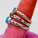 Details of hand engraved star settings on three rings created by Corkie Bolton Jewelry. The rings sit on a neon velvet ring holder.