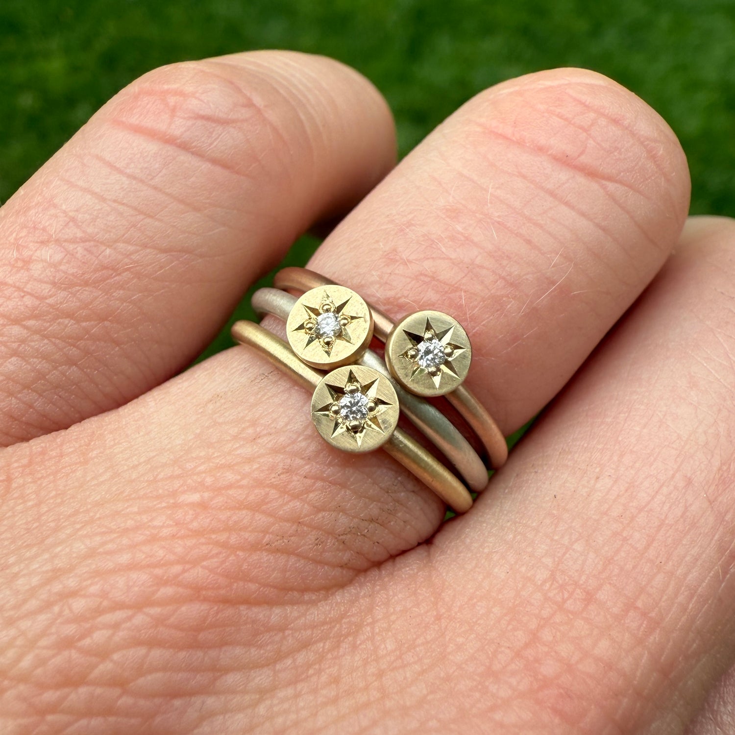 Stack of all the metal options including silver, 14k yellow and 14k rose gold bands all with a 14k yellow gold disc, hand engraved with a diamond star setting.

