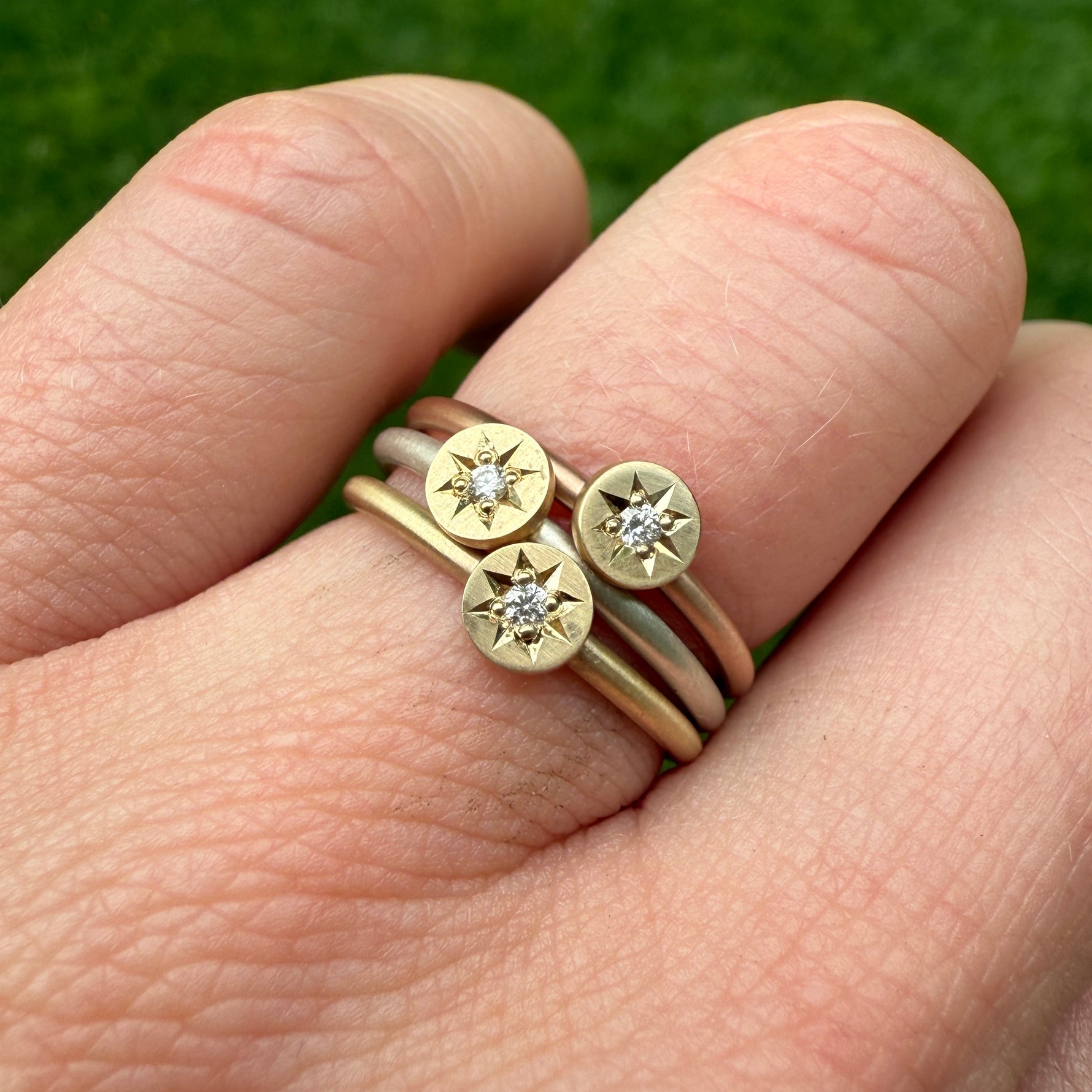 Stack of all the metal options including silver, 14k yellow and 14k rose gold bands all with a 14k yellow gold disc, hand engraved with a diamond star setting.

