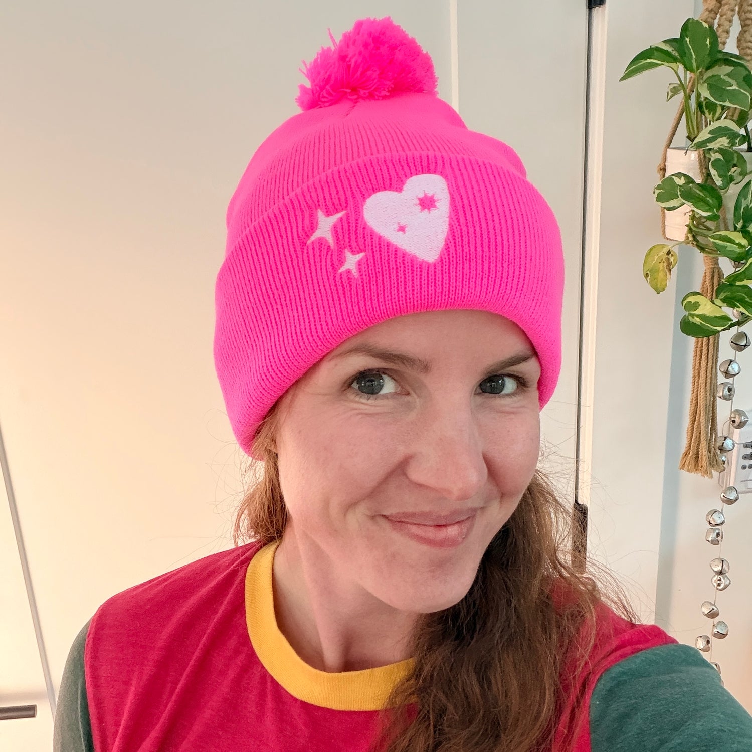 Jeweler wearing a neon pink pom-pom beanie embroidered with a white Misfit Heart and sparkles, styled casually for a fun, creative look.