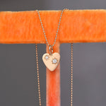 Gold heart-shaped pendant necklace with diamonds on an orange stand against a gray background
