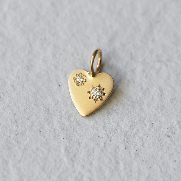 A 14k gold heart with two diamonds. It has been hand engraved by Corkie Bolton Jewelry.