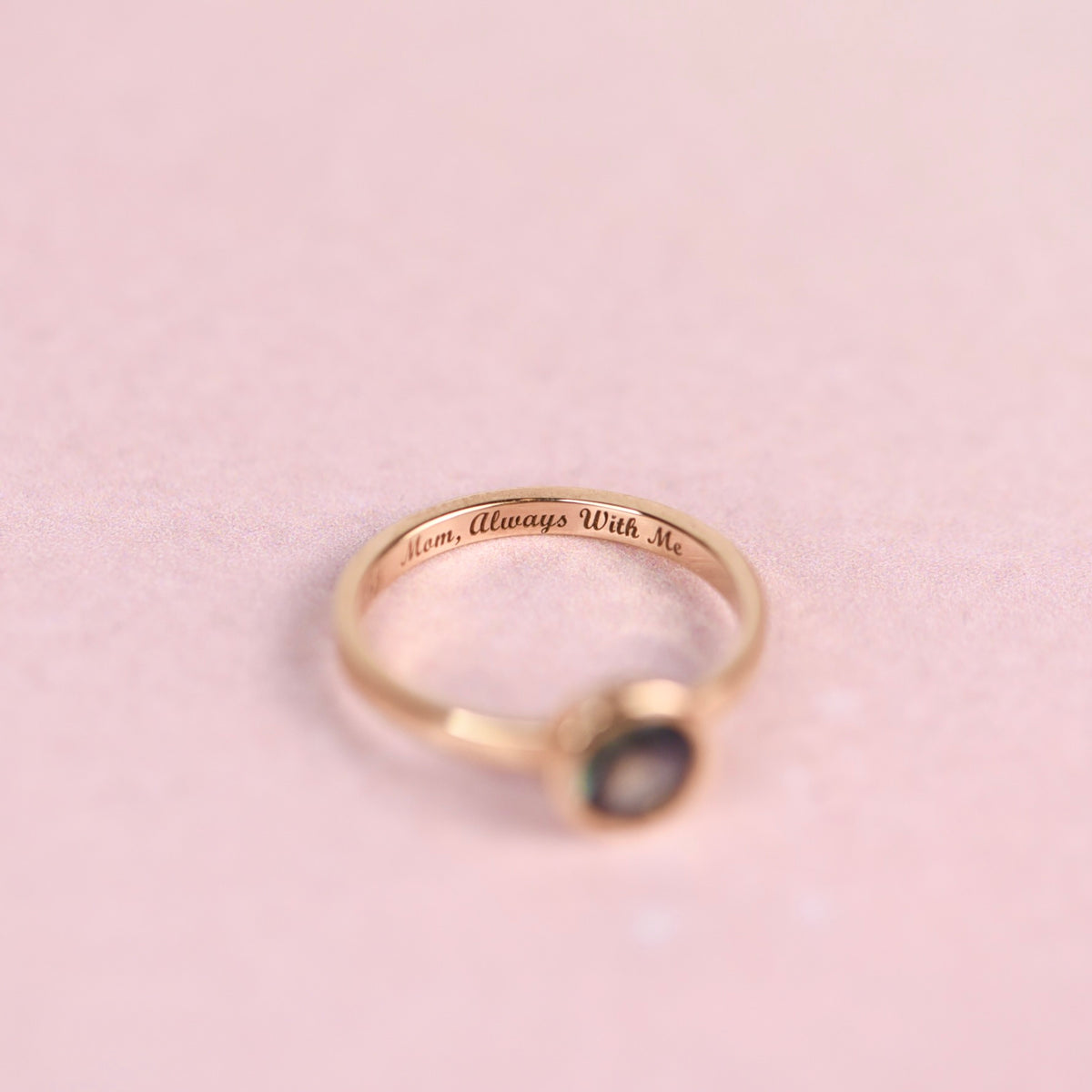 Inside of a gold ring band engraved with “Mom, Always With Me” in script lettering