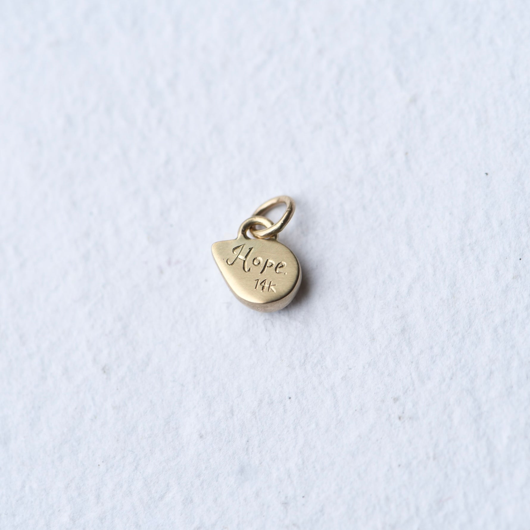 The backside of 1 teardrop flashy opal set in 14k gold as a charm. It is hand engraved with the word HOPE and 14K