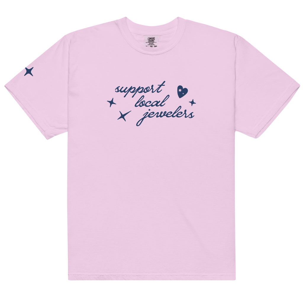 Light purple (orchid), short-sleeve T-shirt with a navy blue design on the front. The design includes the phrase "support local jewelers" in cursive font, accompanied by small star-like shapes and a heart with a sparkle inside. A small star detail is featured on the left sleeve.